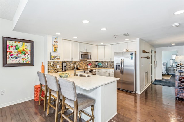 kitchen with dark wood finished floors, stainless steel appliances, baseboards, white cabinetry, and a peninsula