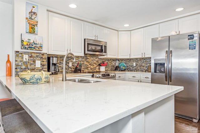 kitchen with stainless steel appliances, white cabinetry, a sink, and a peninsula