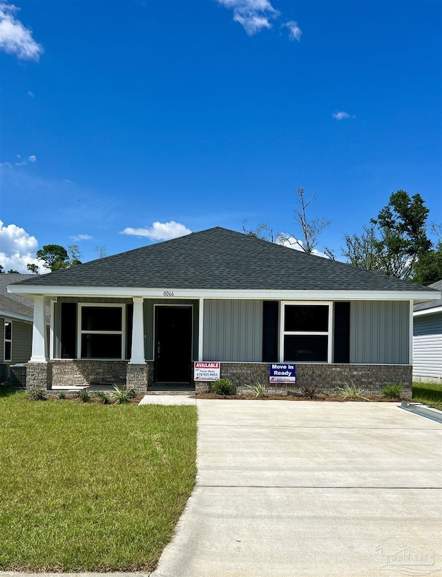 view of front of property featuring brick siding, roof with shingles, a porch, and a front yard