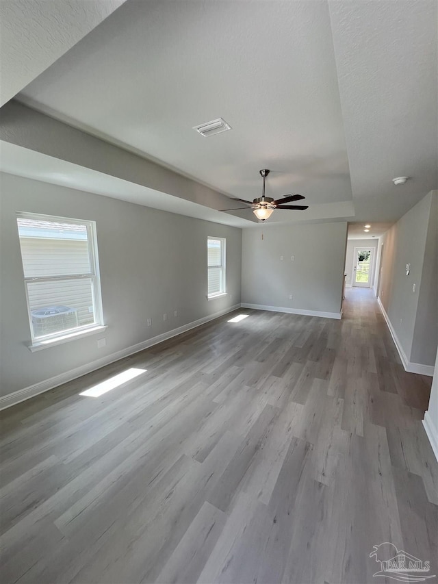 empty room featuring a ceiling fan, visible vents, baseboards, and wood finished floors