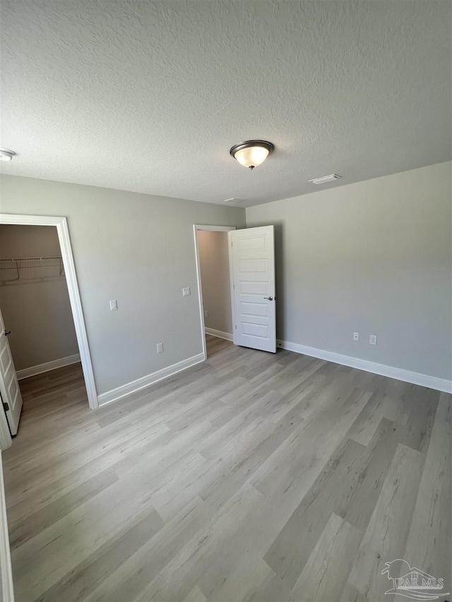 unfurnished bedroom with light wood-style floors, a spacious closet, baseboards, and a textured ceiling