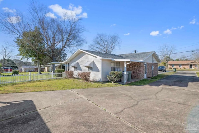 view of property exterior featuring driveway, fence, a lawn, and brick siding