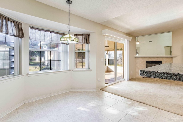 unfurnished dining area featuring plenty of natural light, ceiling fan, a textured ceiling, and a tile fireplace