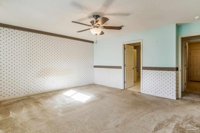 spare room with a textured ceiling, light colored carpet, ceiling fan, and ornamental molding