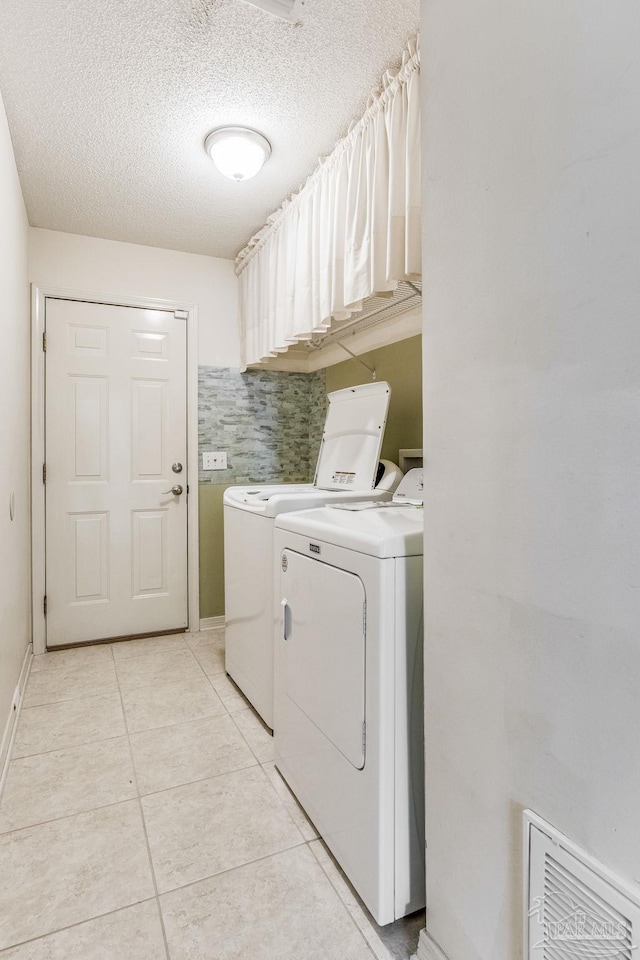 clothes washing area featuring light tile patterned flooring, a textured ceiling, and washing machine and clothes dryer