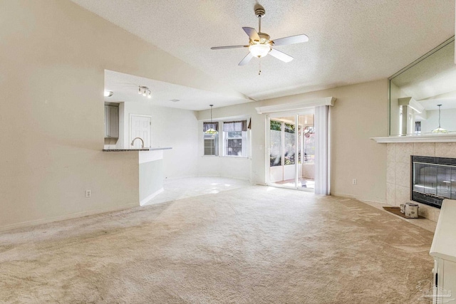 unfurnished living room featuring light carpet, a textured ceiling, vaulted ceiling, ceiling fan, and a tile fireplace