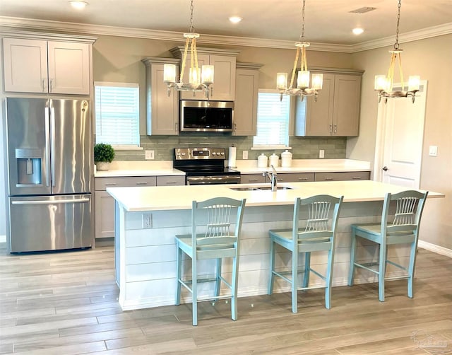 kitchen featuring a breakfast bar, stainless steel appliances, a kitchen island with sink, sink, and hanging light fixtures