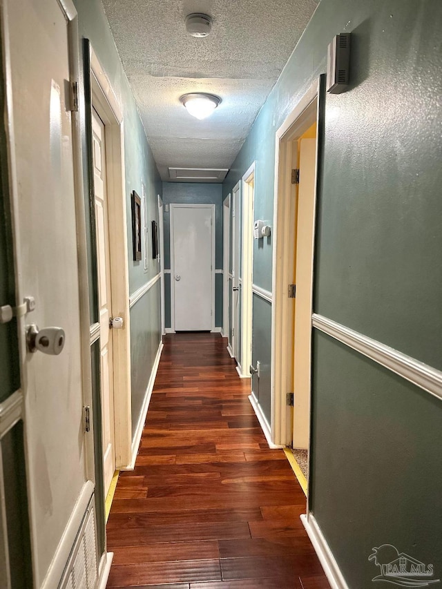 corridor with dark hardwood / wood-style floors and a textured ceiling