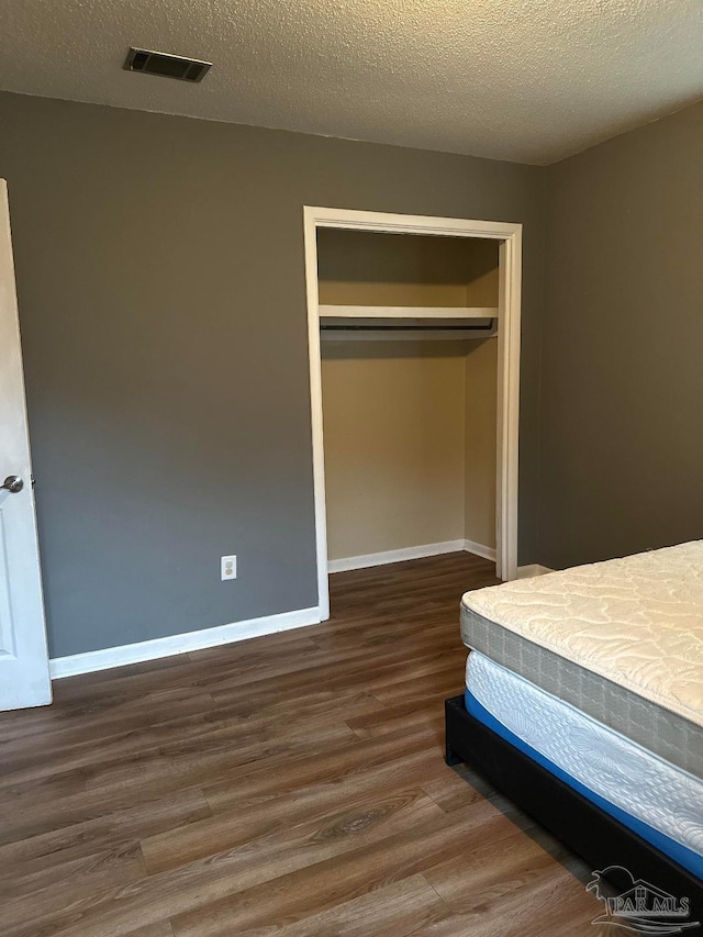 unfurnished bedroom featuring dark wood-type flooring, a closet, and a textured ceiling