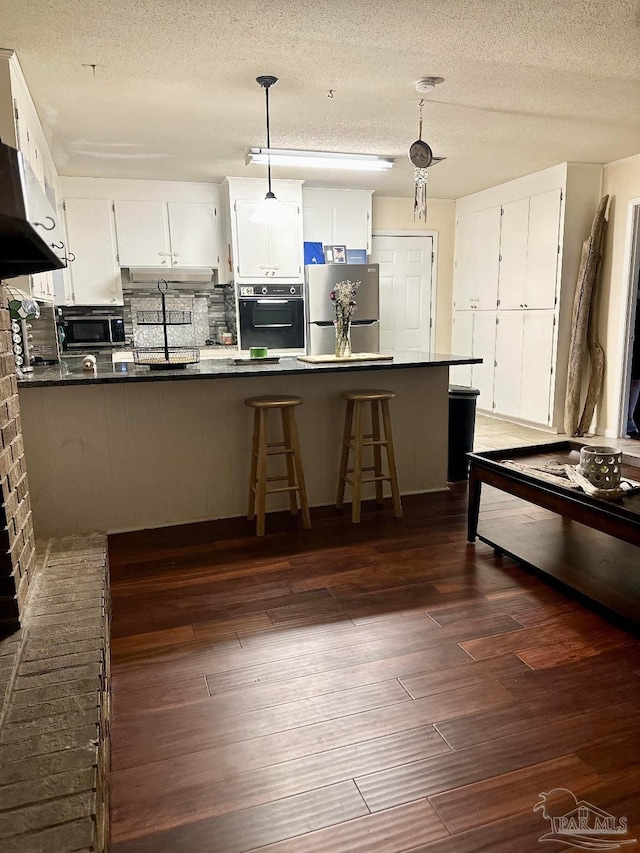 kitchen featuring decorative light fixtures, appliances with stainless steel finishes, dark hardwood / wood-style flooring, kitchen peninsula, and white cabinets