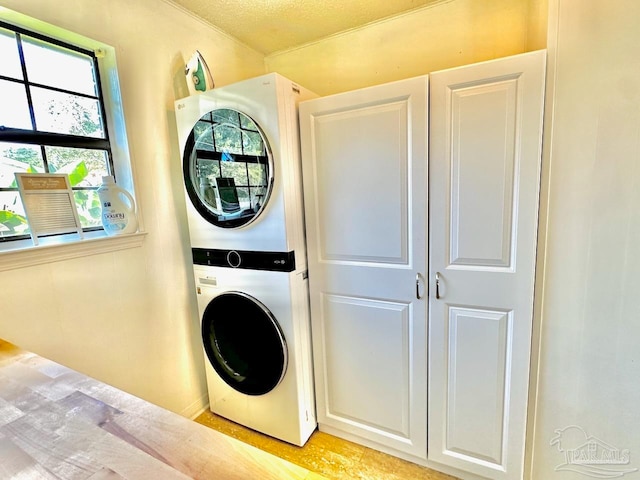 clothes washing area featuring stacked washer / drying machine, cabinets, and a textured ceiling