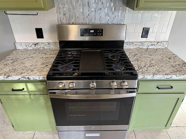 kitchen featuring tasteful backsplash, light stone counters, green cabinetry, and stainless steel gas range