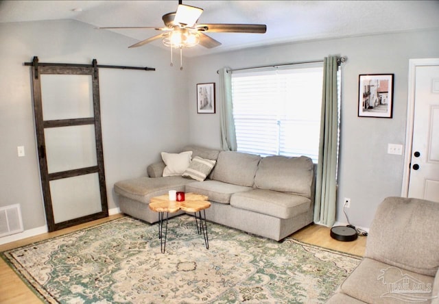 living room featuring a barn door, ceiling fan, hardwood / wood-style floors, and vaulted ceiling