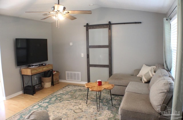 living room with a barn door, light hardwood / wood-style flooring, ceiling fan, and vaulted ceiling