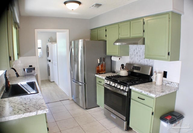 kitchen featuring sink, stainless steel appliances, stacked washer / dryer, decorative backsplash, and green cabinetry