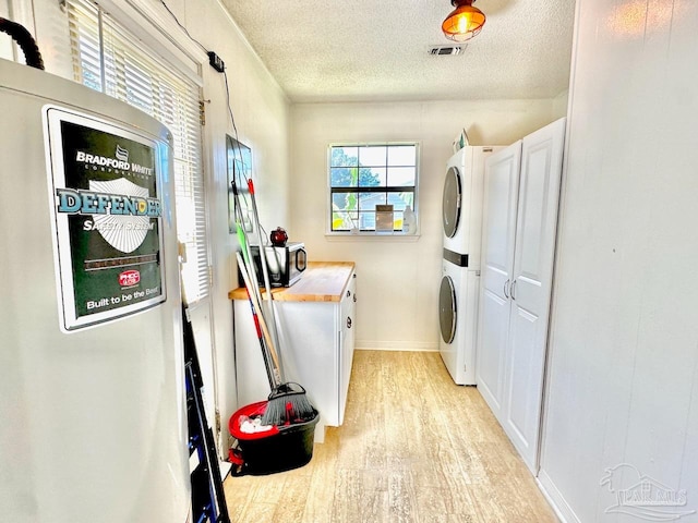 laundry room with a textured ceiling, light hardwood / wood-style flooring, cabinets, and stacked washer / drying machine