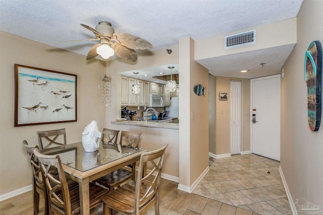 dining area featuring a textured ceiling, visible vents, a ceiling fan, and baseboards