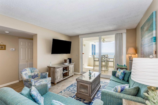 living area with a textured ceiling, light wood-style flooring, and baseboards