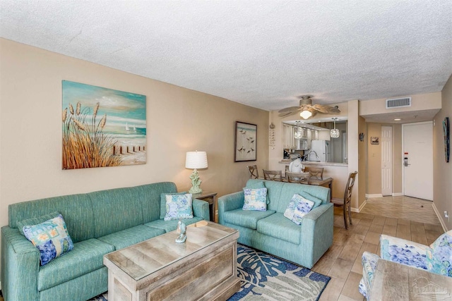 living room featuring a textured ceiling, visible vents, a ceiling fan, and light wood-style floors