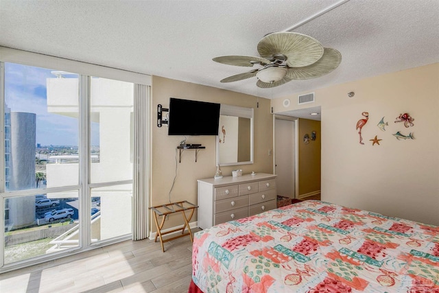 bedroom with light wood finished floors, a textured ceiling, visible vents, and a ceiling fan