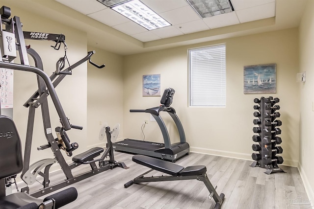exercise area with wood finished floors, a tray ceiling, and baseboards