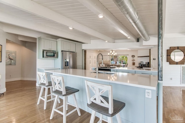 kitchen featuring a sink, beam ceiling, light wood-type flooring, and stainless steel appliances