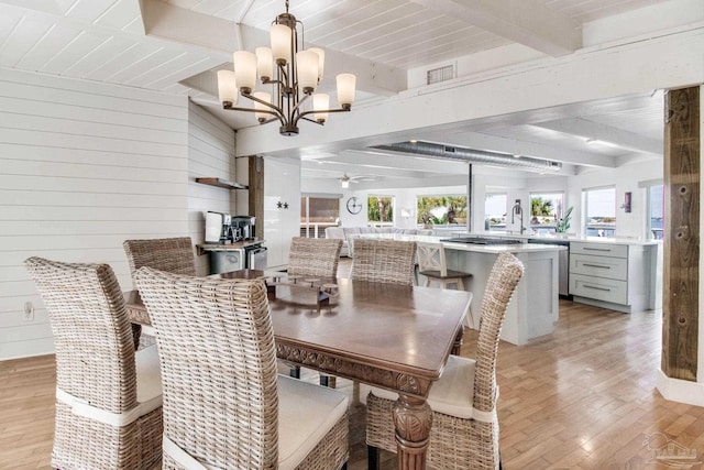 dining room featuring visible vents, beam ceiling, ceiling fan with notable chandelier, light wood-style floors, and wood walls