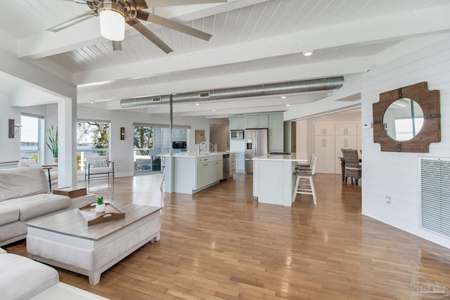 living room featuring visible vents, wooden walls, ceiling fan, light wood-type flooring, and beam ceiling