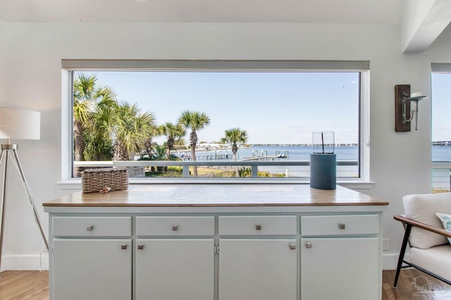 kitchen with baseboards, a water view, light countertops, and light wood finished floors