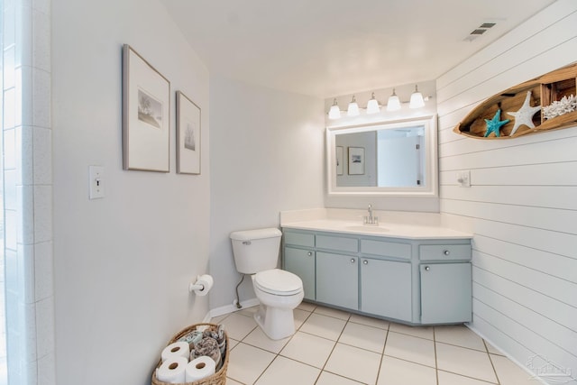 bathroom featuring visible vents, toilet, wooden walls, tile patterned flooring, and vanity