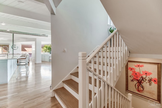 stairway with beam ceiling, wood finished floors, and baseboards