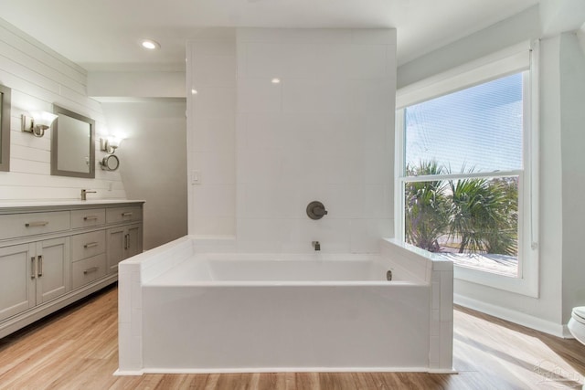 bathroom with baseboards, wood finished floors, a bath, and vanity