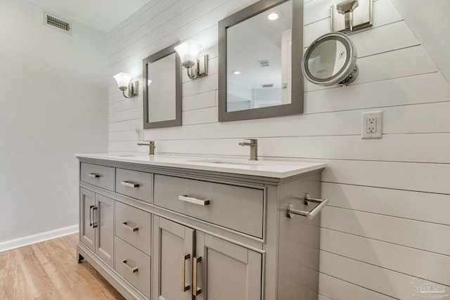 bathroom featuring visible vents, wood walls, double vanity, wood finished floors, and a sink