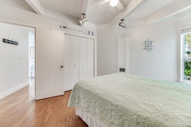 bedroom featuring baseboards, beamed ceiling, light wood-type flooring, wooden ceiling, and a closet