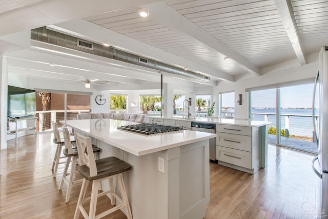 kitchen with light wood-type flooring, beamed ceiling, a spacious island, open floor plan, and appliances with stainless steel finishes