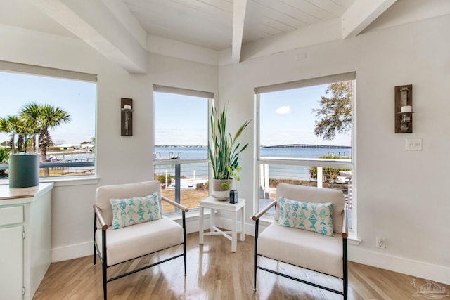 living area featuring beamed ceiling, a water view, baseboards, and light wood-style flooring