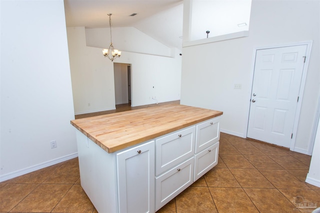 kitchen with pendant lighting, butcher block countertops, white cabinetry, dark tile patterned flooring, and an inviting chandelier