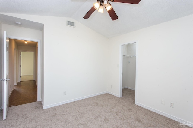 unfurnished bedroom with lofted ceiling, ceiling fan, light carpet, a walk in closet, and a closet