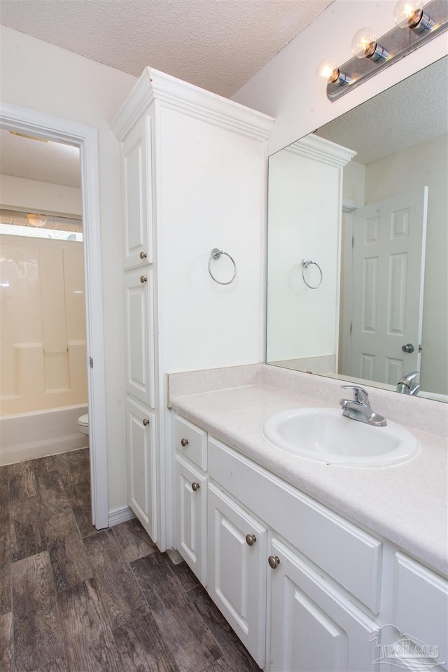 full bathroom featuring toilet, wood-type flooring,  shower combination, a textured ceiling, and vanity