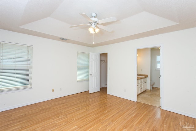 unfurnished bedroom featuring a tray ceiling, light hardwood / wood-style floors, ceiling fan, and ensuite bathroom