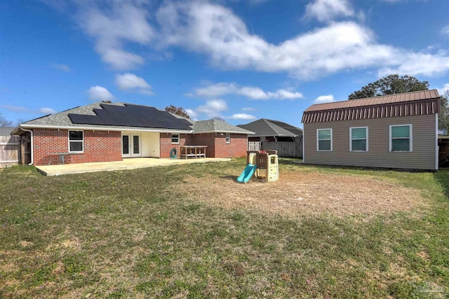 rear view of property featuring a playground, a yard, a patio area, and solar panels