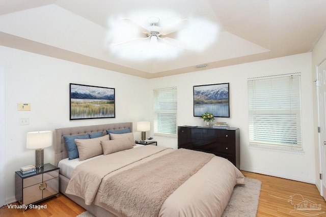 bedroom featuring a raised ceiling, ceiling fan, and light hardwood / wood-style flooring