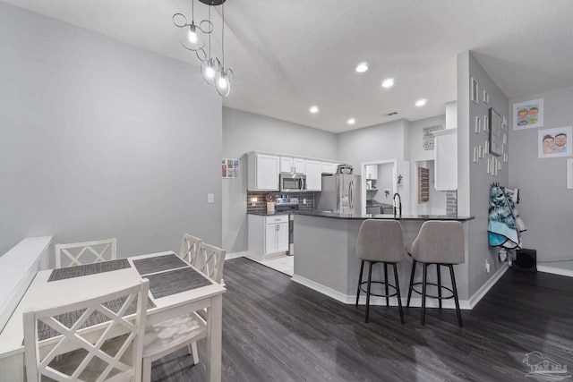 kitchen featuring appliances with stainless steel finishes, white cabinets, dark hardwood / wood-style flooring, decorative light fixtures, and kitchen peninsula