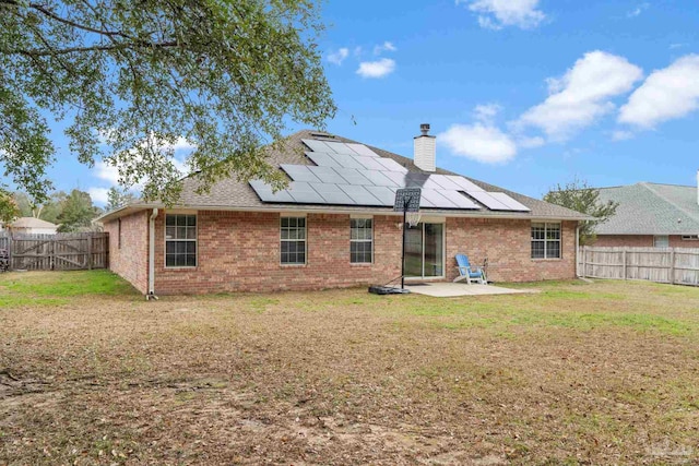 rear view of property with a patio, a lawn, and solar panels