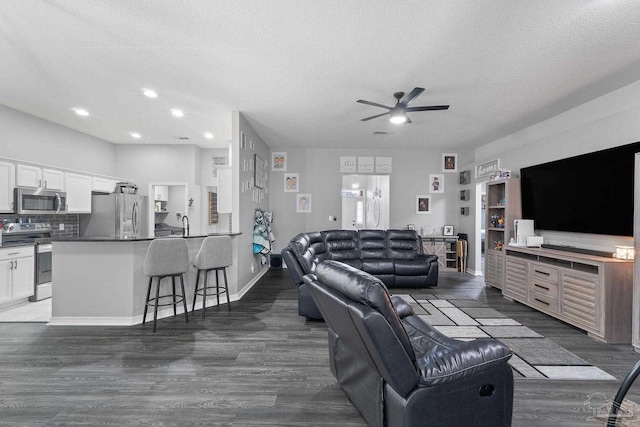 living room featuring ceiling fan, dark wood-type flooring, and a textured ceiling