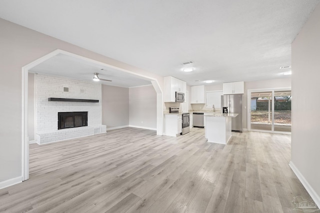 unfurnished living room with ceiling fan, sink, light hardwood / wood-style floors, and a brick fireplace