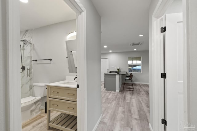 bathroom with a tile shower, vanity, hardwood / wood-style flooring, and toilet