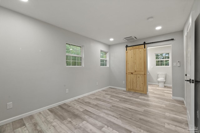 unfurnished bedroom with a barn door, ensuite bathroom, and light wood-type flooring