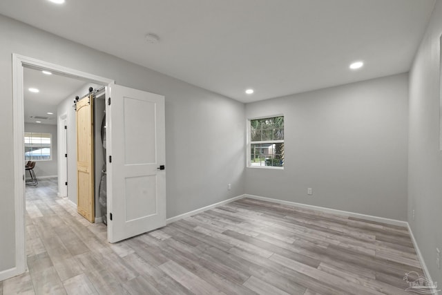 unfurnished room with a barn door and light wood-type flooring