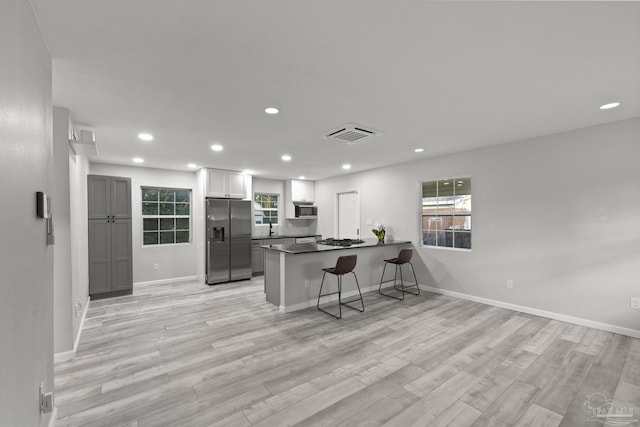 kitchen featuring white cabinetry, stainless steel appliances, kitchen peninsula, light hardwood / wood-style floors, and a kitchen bar